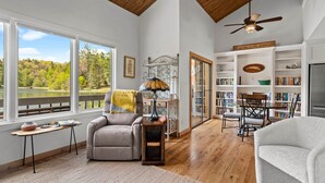 A spacious living room with a large window overlooking a lake, a fireplace, a bookshelf, and a dining area. - Lakeside Serenity, Lakeside Serenity (Jackson County)