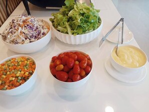 A table with various food items including a salad, a bowl of cherry tomatoes, a bowl of mixed vegetables, and a bowl of sauce. - P.T. Grand Hotel (Kanchanaburi)