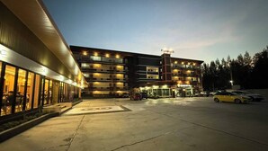 A multi-story hotel with a central entrance, a parking lot, and a dining area visible through the windows. - P.T. Grand Hotel (Kanchanaburi)