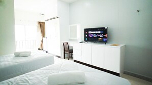 A hotel room with two beds, a desk with a TV displaying streaming services, a chair, and a window with curtains. - P.T. Grand Hotel (Kanchanaburi)