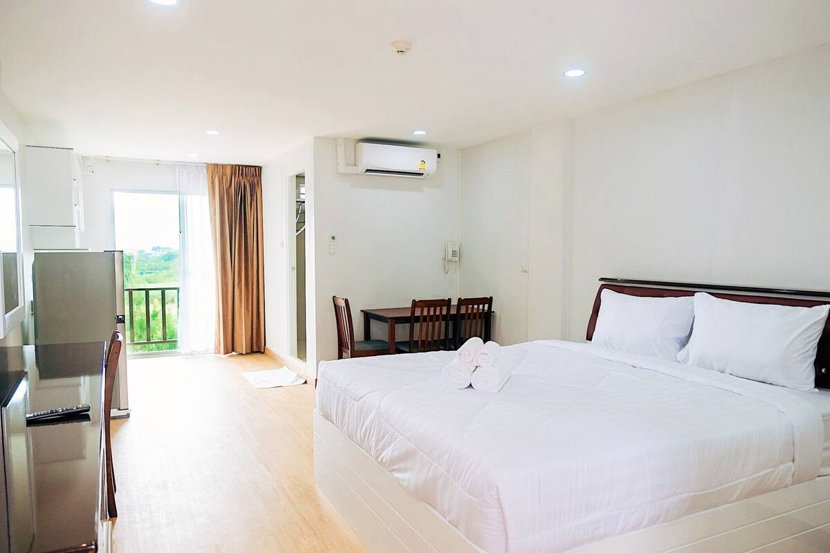 A hotel room with a bed, a desk, chairs, an air conditioning unit, and a balcony.