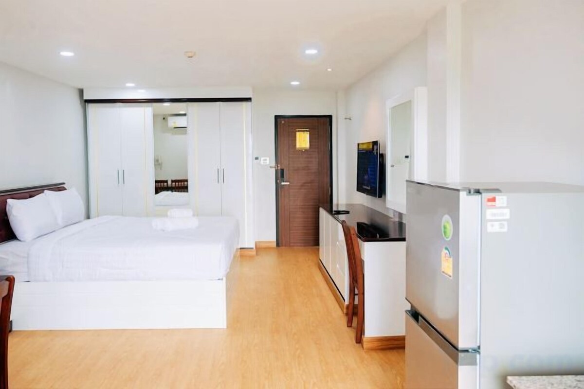 A hotel room with a bed, a desk, a refrigerator, and a television.