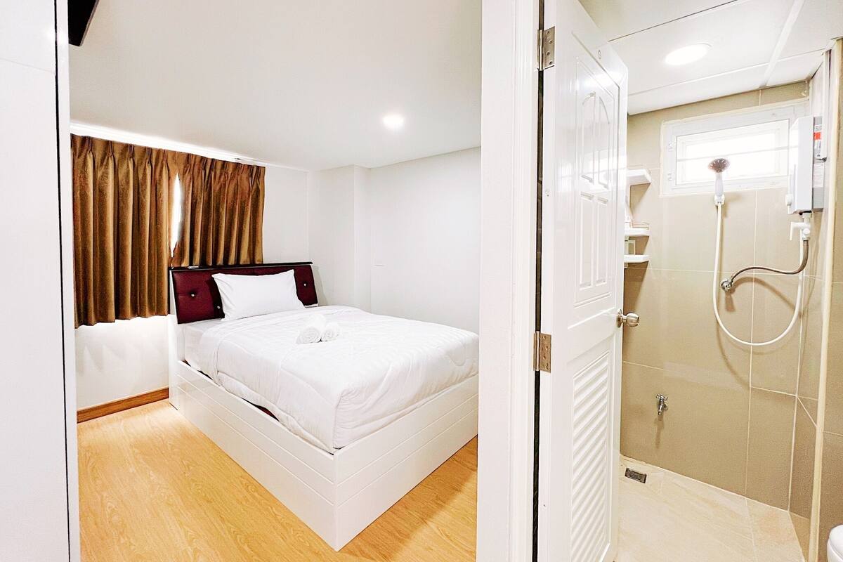 A hotel room with a bed, a bathroom with a shower, and a window with curtains.