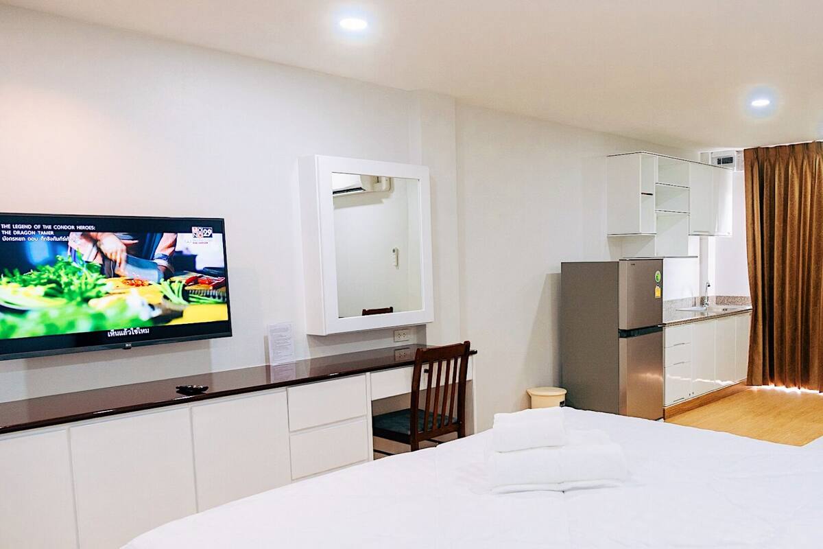 A hotel room with a bed, a TV, a small kitchenette, and a bathroom.