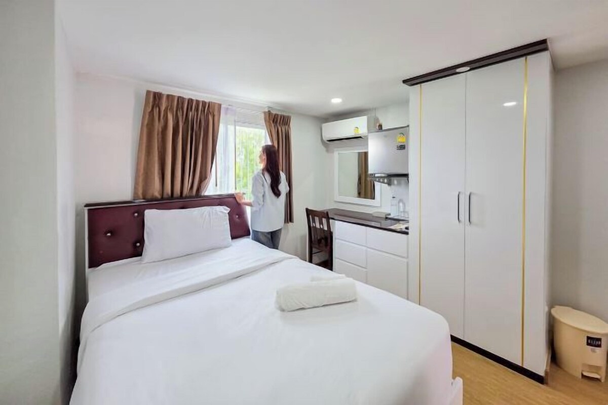 A hotel room with a bed, a desk, a wardrobe, and a window with curtains.