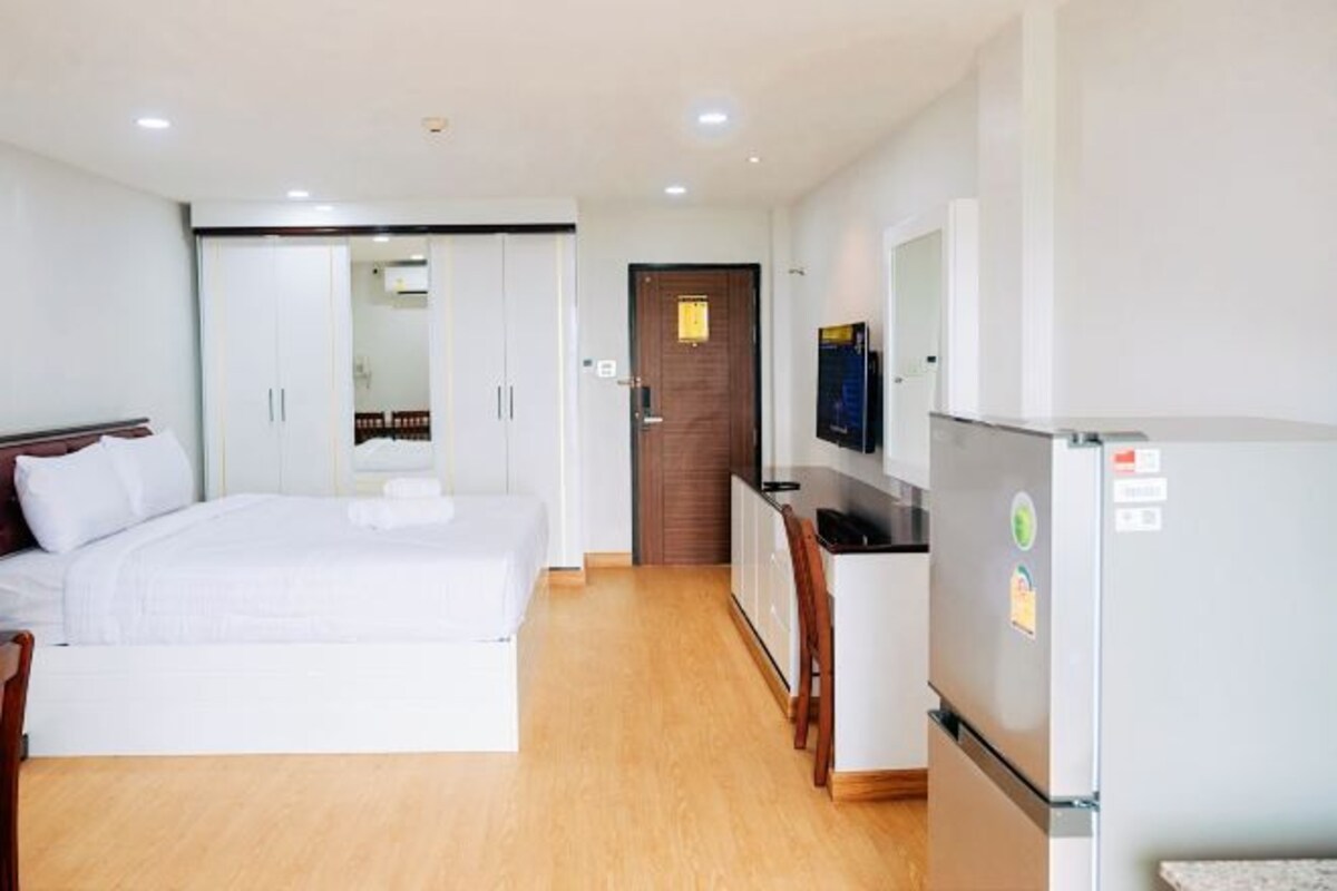 A hotel room with a bed, a small kitchenette, a TV, and a wooden floor.