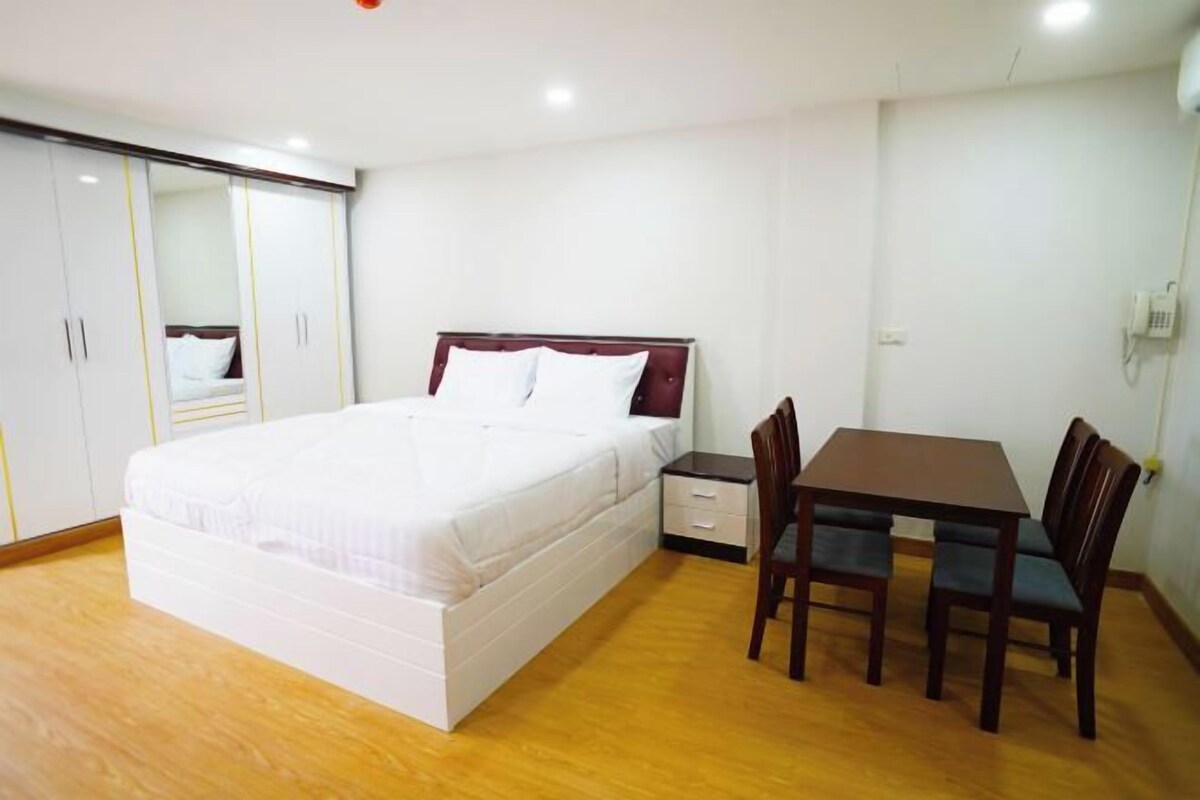 A bedroom with a bed, a bedside table, a chair, a desk, and a wardrobe.