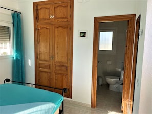 Una camera da letto con un letto, un armadio in legno e un bagno visibile attraverso una porta aperta.