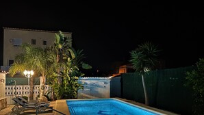 Une piscine dont le bord est recouvert de carreaux, entourée de dalles de pierre et agrémentée d’une petite terrasse avec des chaises longues.