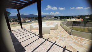 A rooftop terrace with stone flooring, white outdoor furniture, and a view of distant mountains and buildings. - Beautiful house in Campeche for up to 16 people, heated pool and spa. (Florianópolis)