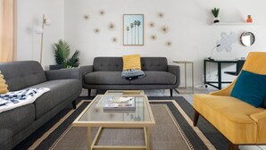 A modern living room with a grey sofa, a yellow armchair, and a glass coffee table. - Posh Old Village Townhome | Stylish Escape (Mount Pleasant)