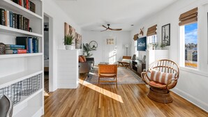Una sala de estar amplia con pisos de madera, una gran estantería, un sillón cómodo y un ventilador de techo.