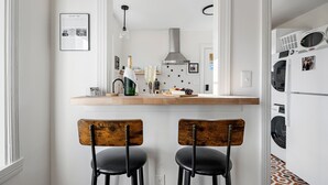 Una cocina con encimera de madera, dos sillas, una lámpara colgante y una lavadora al fondo.