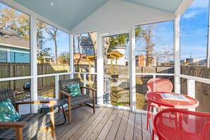 Una terrazza coperta all'aperto con sedie in vimini e metallo, un tavolo e vista su un giardino privato con recinzione in legno e una casa.