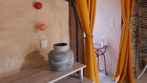 Quarto com parede de pedra, teto de madeira, uma mesa com um vaso e cortinas amarelas.