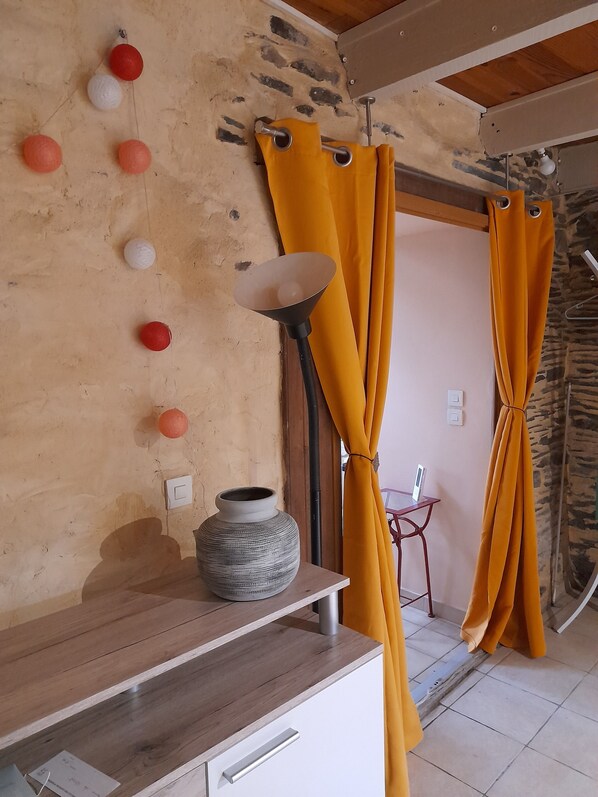 A room with a stone wall, a wooden ceiling, a table with a vase, and yellow curtains. - A charming house surrounded by nature (Paule)