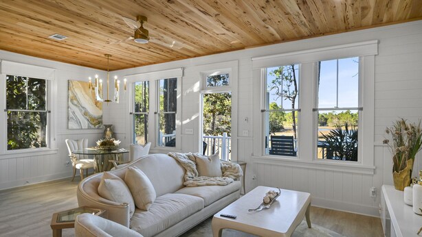 A spacious living room with a wooden ceiling, large windows, a beige sofa, and a glass coffee table. - ★Luxuriously Romantic One-Of-A-Kind Treehouse w/Canoe, Fire Pit and More★ (Santa Rosa Beach)
