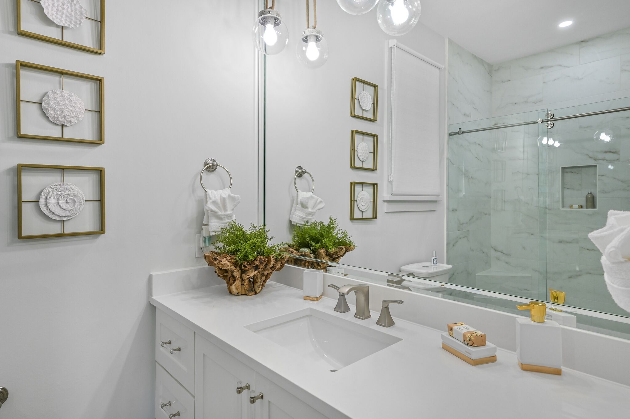 A modern bathroom with a large mirror, white sink, and two towel rings.