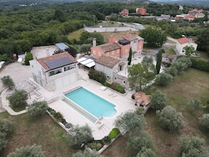 A villa with a swimming pool, stone buildings, and surrounding greenery.