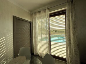 A room with a sliding glass door, a dining table with chairs, and a view of a swimming pool.