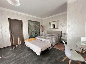 A bedroom with a bed, a desk, a chair, a door, and a painting on the wall.