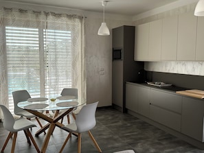 A modern kitchen with a dining area, featuring a glass-top table, white chairs, and grey cabinets.