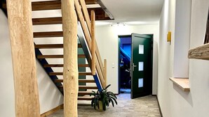 Un pasillo con una escalera de madera, una puerta verde y una planta en maceta.