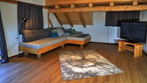 Una sala de estar acogedora con techo de madera, un sofá modular, un televisor sobre un mueble de madera y una alfombra grande de madera para el suelo.