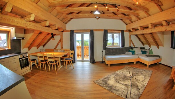 Un interior acogedor de madera, con zona de comedor, un sofá y un ventanal grande.