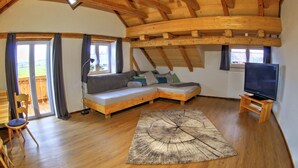 Una sala de estar acogedora con techo de madera, un sofá modular, un televisor y un ventanal grande.