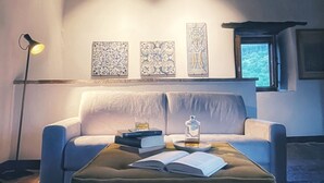 Un salon chaleureux avec un canapé, une table basse sur laquelle sont posés des livres et un verre, et une lampe. Trois panneaux décoratifs ornent le mur.