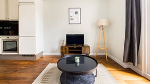 A modern living room with a round black coffee table, a small potted plant, a television on a wooden stand, and a floor lamp. - The Chelsea Collection (London)