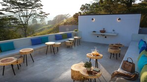 A rooftop patio with round wooden tables, a seating area with cushions, and a white wall with shelves. - Misty Villa by The Serendipity Collection (Ambagamuwa)