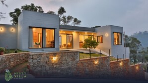 A modern villa with a stone facade, large windows, and a well-lit interior. - Misty Villa by The Serendipity Collection (Ambagamuwa)