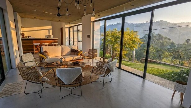 A modern living room with a large window, a sofa, chairs, and a coffee table. - Misty Villa by The Serendipity Collection (Ambagamuwa)