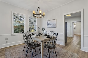Une salle à manger avec une table en bois, des chaises noires, un lustre et une vue par la fenêtre.