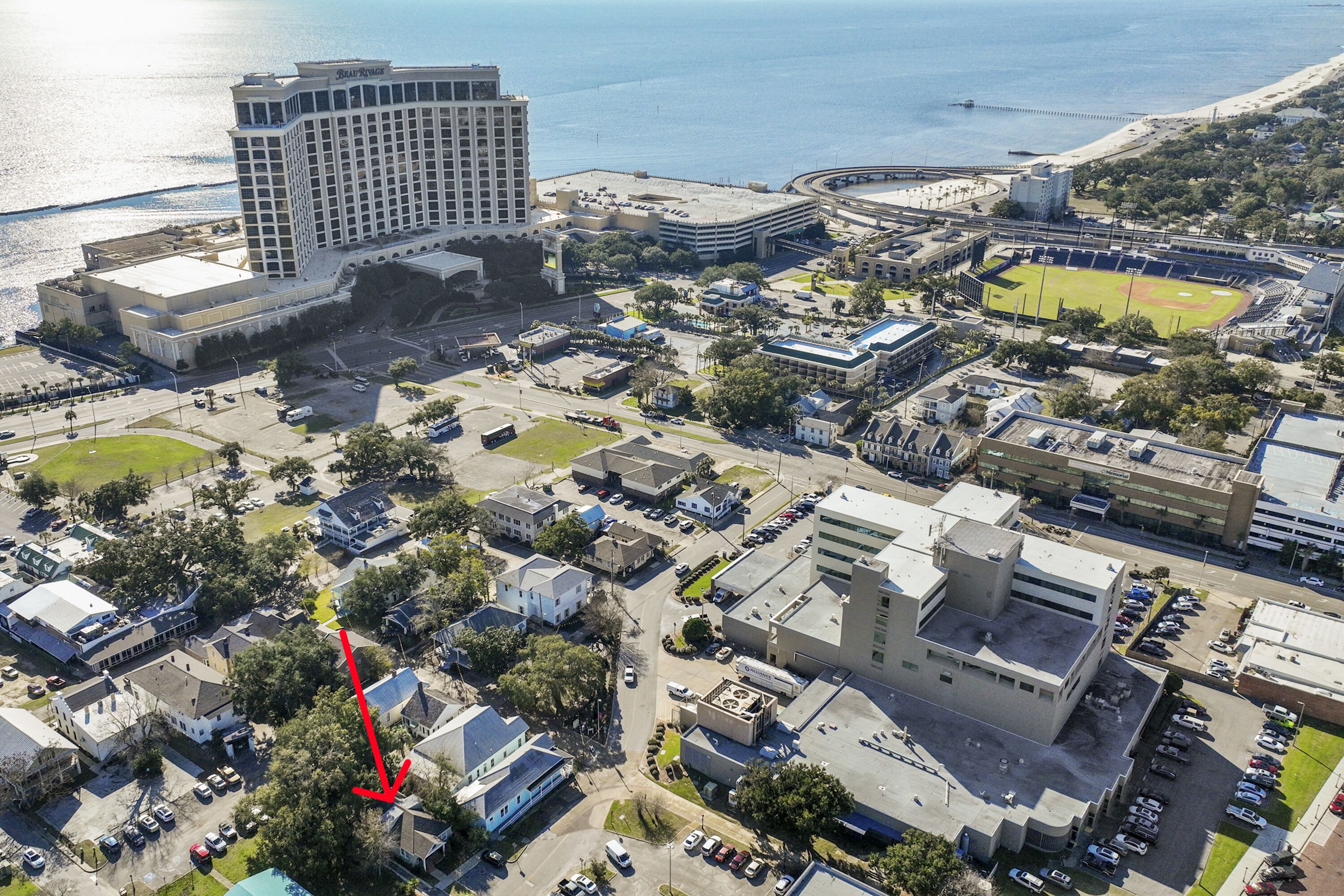 An aerial view of a coastal city with a prominent hotel, a baseball field, and various buildings.