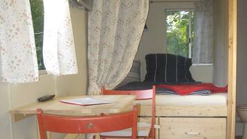 A small bedroom with a single bed, a wooden chair, a desk, and a window with floral curtains.