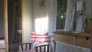 Una habitación acogedora con una silla de madera, una mesita pequeña y un ventanal con cortinas florales.