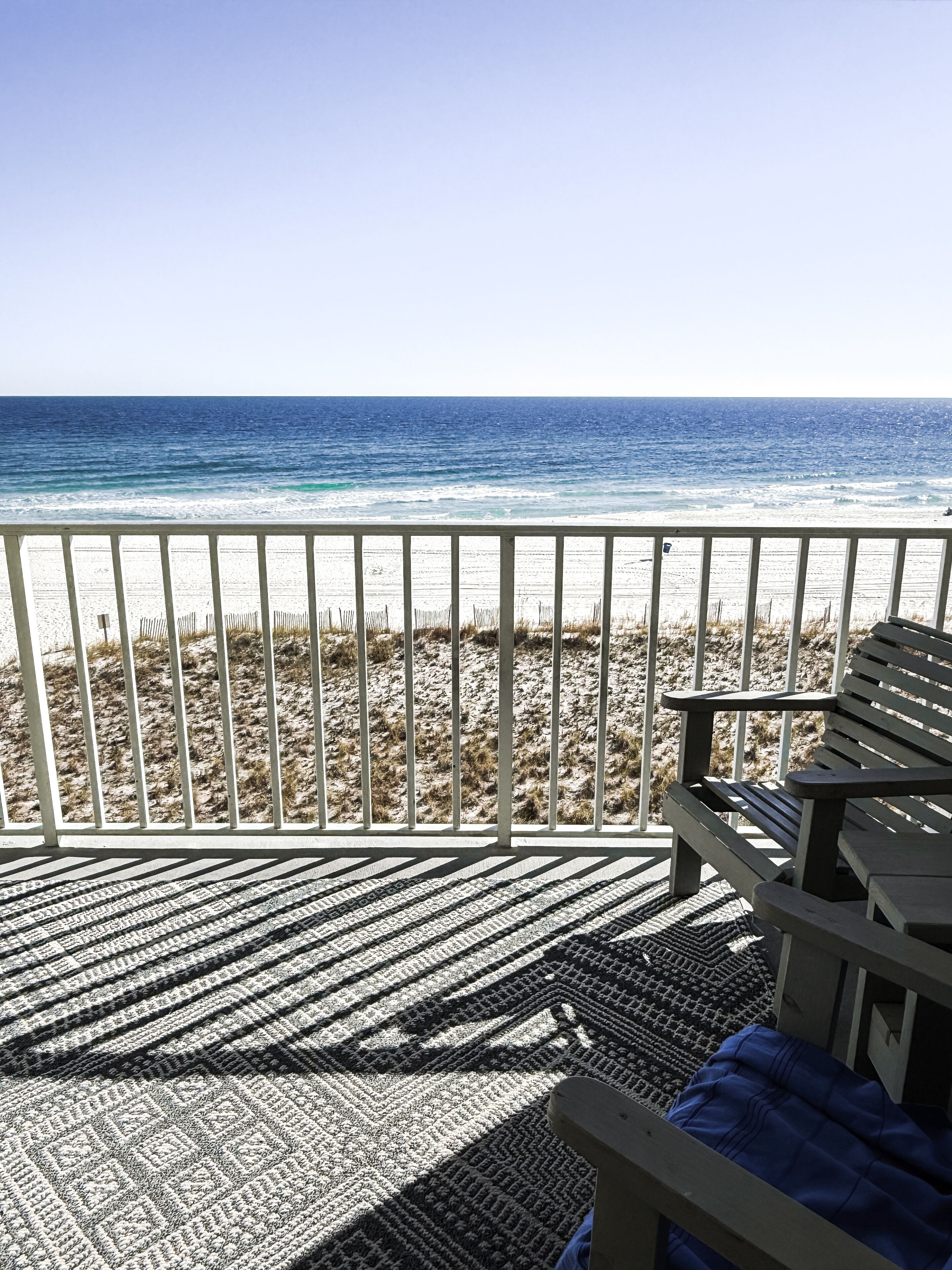 Uitzicht op het strand vanaf een balkon, met een gekleurd tapijt en houten meubels.