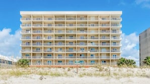 Un hotel de varios pisos con balcones, situado en una playa de arena.