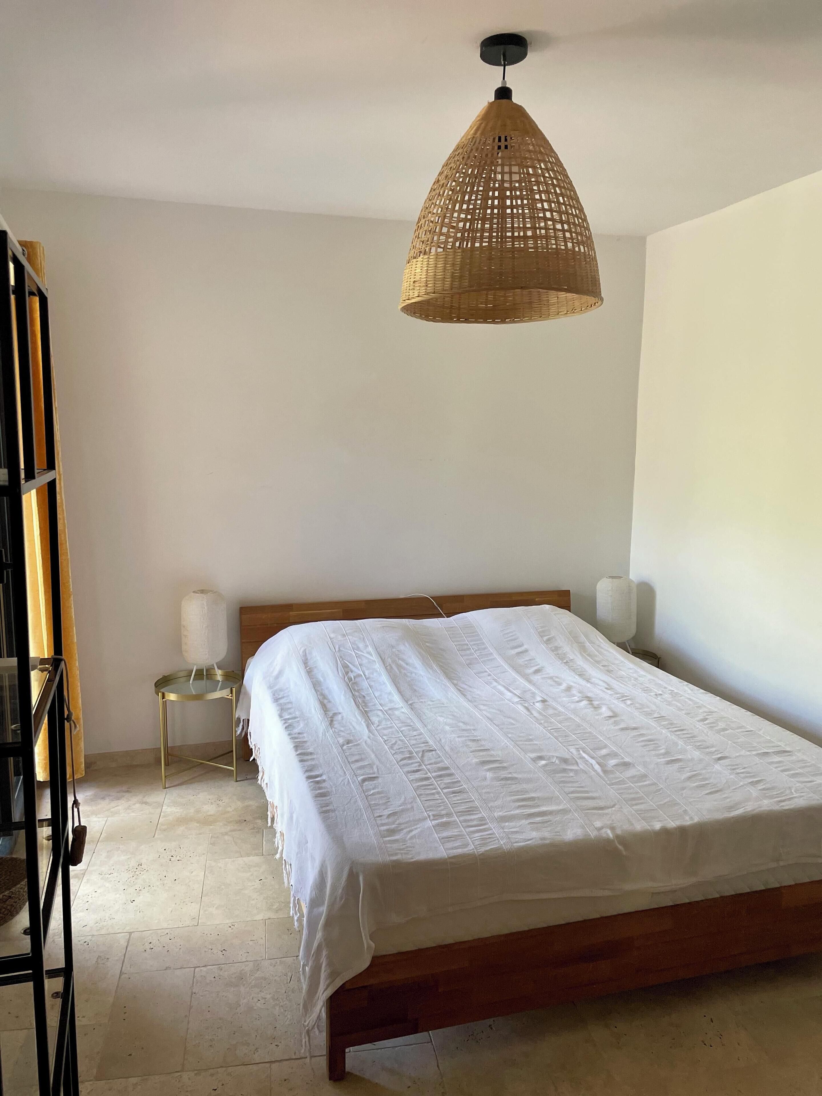A bedroom with a wooden bed, a bedside table, a lamp, and a hanging light fixture.