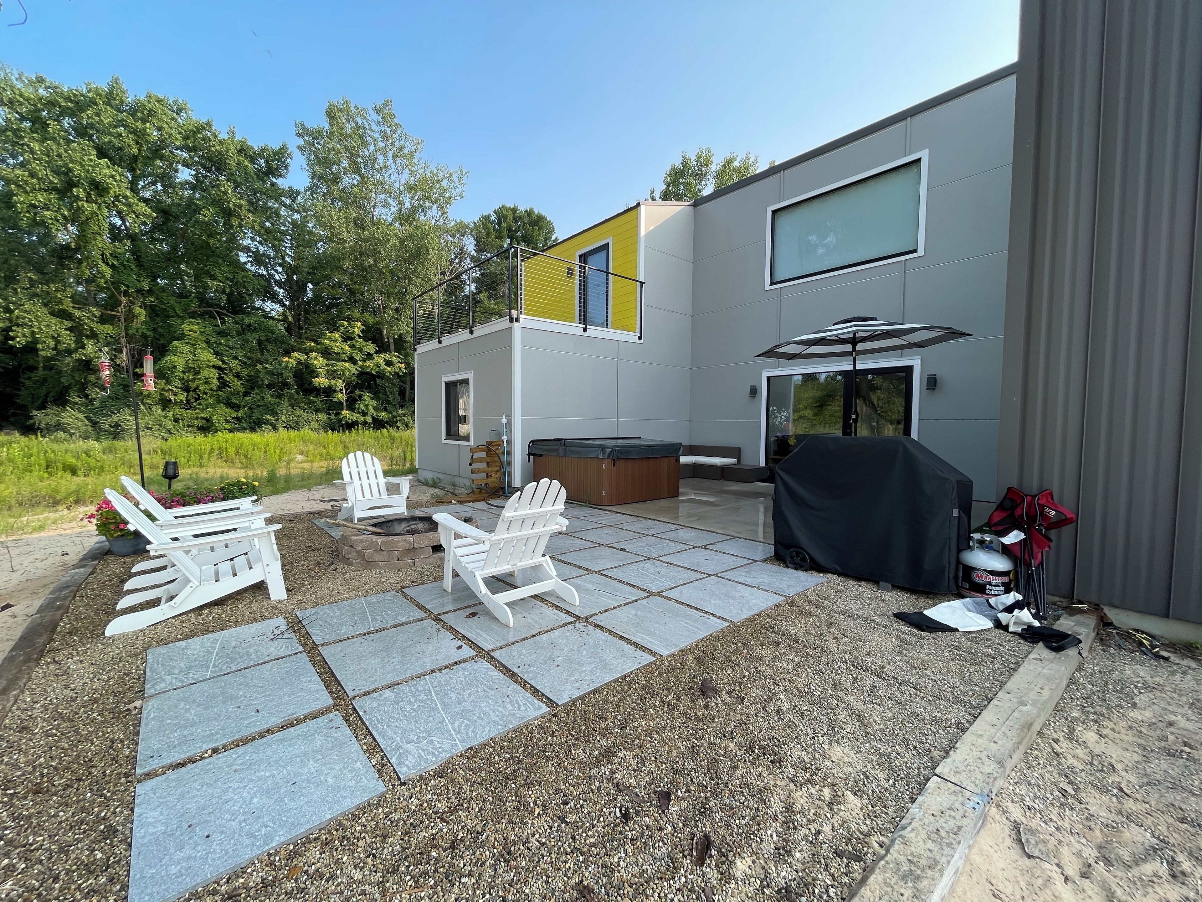A modern outdoor patio with Adirondack chairs, a hot tub, and a barbecue area.