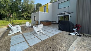 Un patio moderno al aire libre con sillas Adirondack, un jacuzzi y una zona de barbacoa.