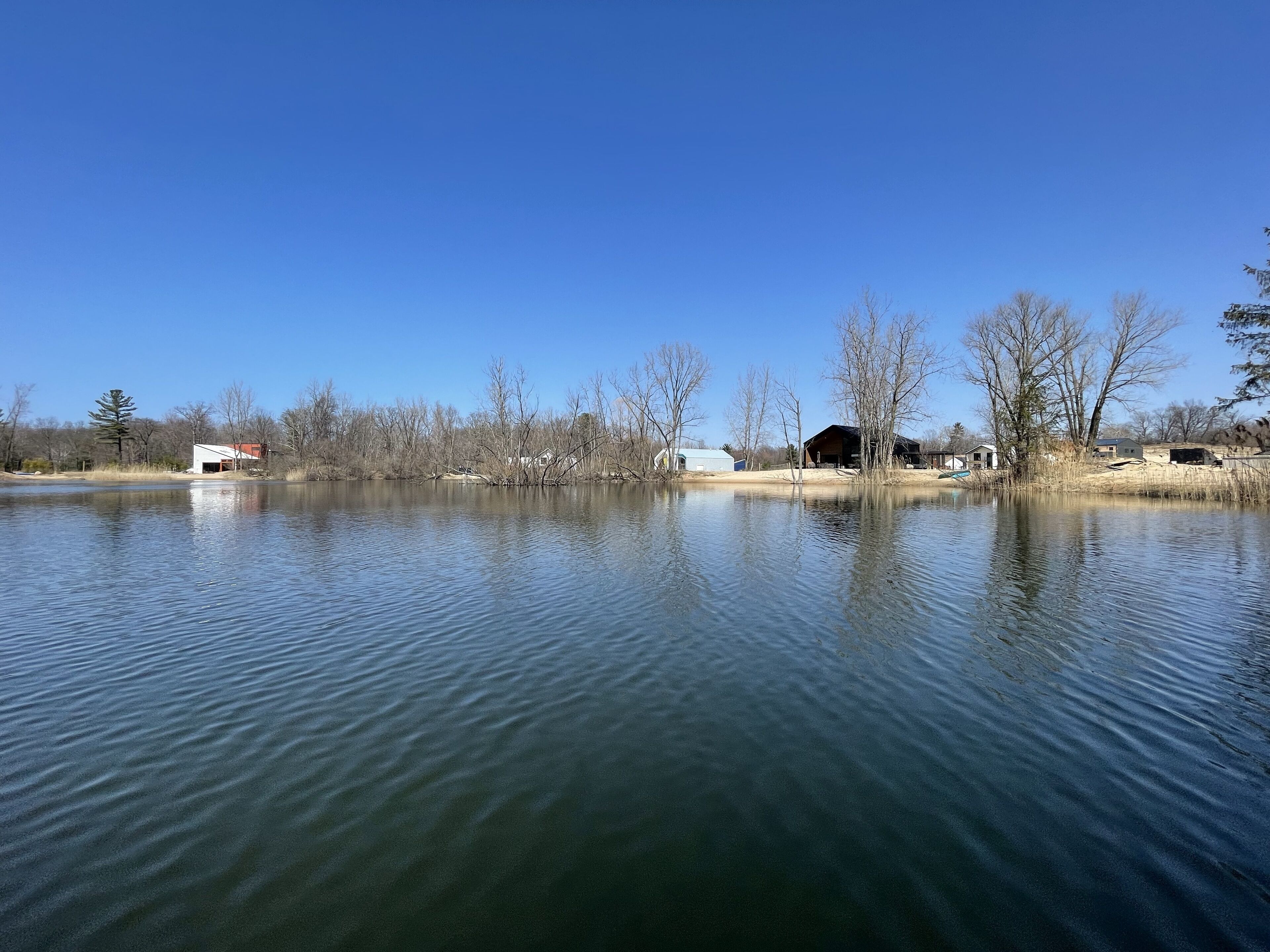 Un lago tranquilo con edificios y árboles al fondo.
