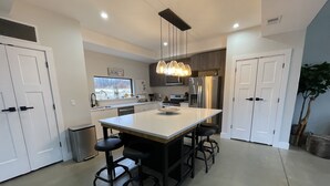 Una cocina moderna con una isla central, taburetes de bar, electrodomésticos de acero inoxidable e iluminación colgante.