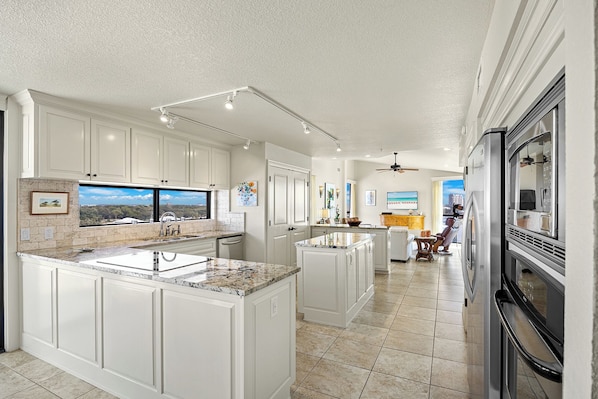 A spacious kitchen with white cabinetry, a large island, and a view of the outdoors.