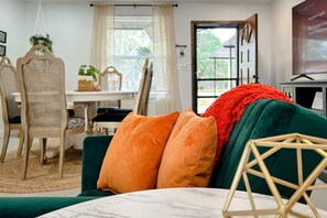 A room with a green sofa, orange cushions, and a wooden geometric decoration.