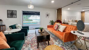 A modern living room with a green sofa, an orange sofa, and a coffee table. There is a view of a pool outside. - Peaceful & stylish pool home with gorgeous lake views (Lake Panasoffkee)