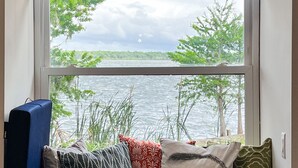 A window seat with a view of a lake and trees, a blue couch, and decorative pillows. - Peaceful & stylish pool home with gorgeous lake views (Lake Panasoffkee)